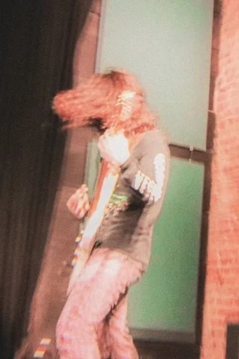 Violet Love mid-song on a small club stage, hair thrown across her face, guitar held low.