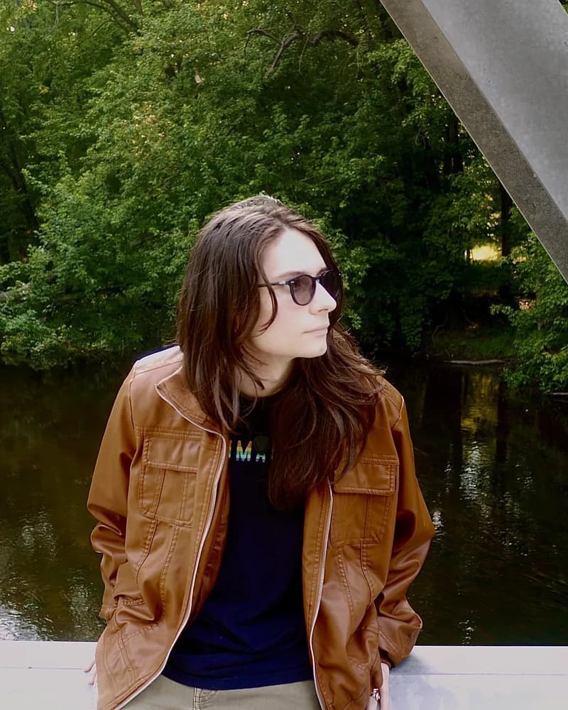 Violet Love in sunglasses and a leather jacket beside a river